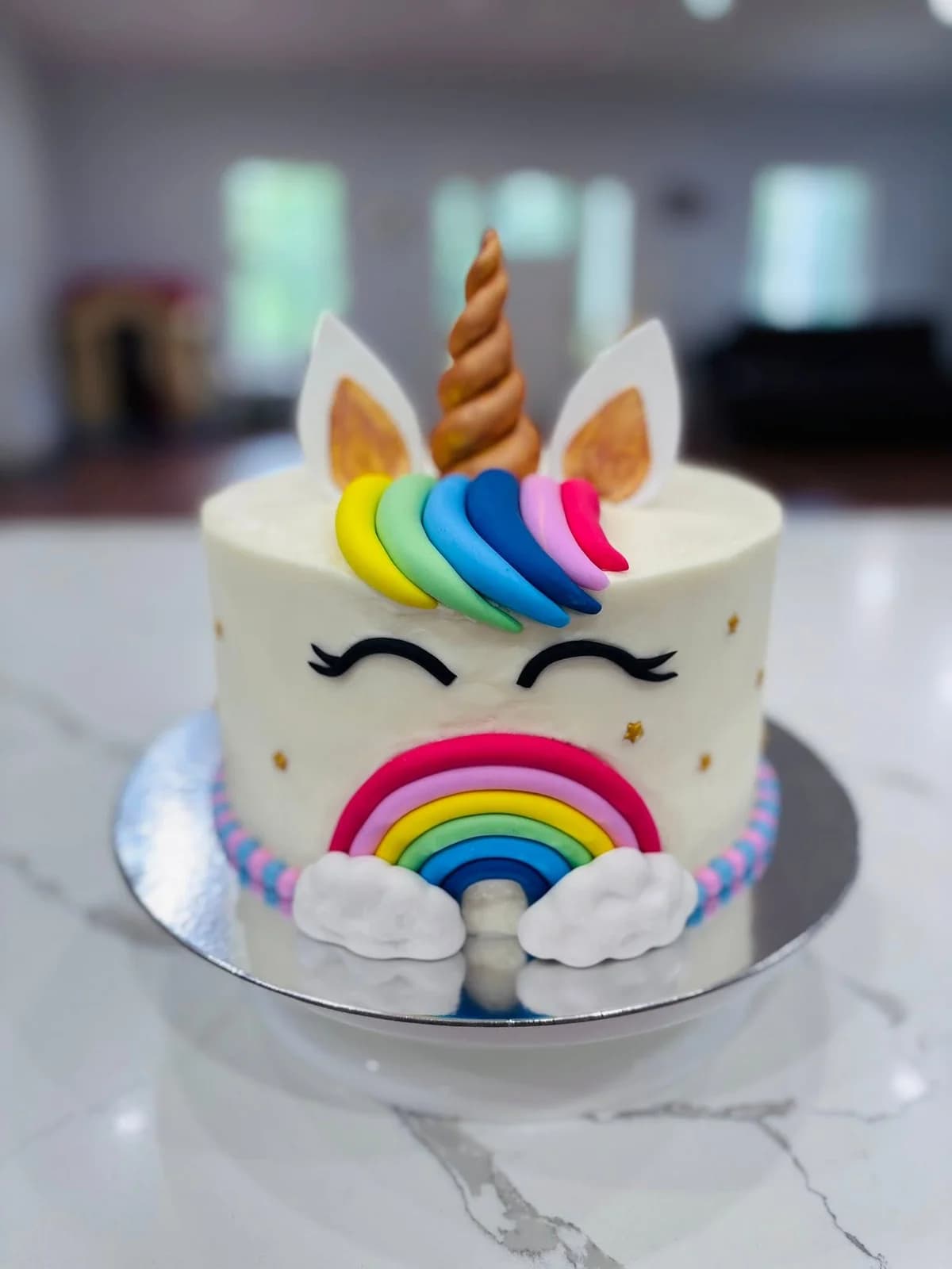 White unicorn cake with a gold horn, rainbow mane and colorful rainbow decoration
